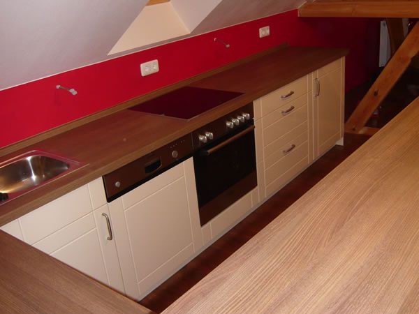 Eine helle, moderne Küche mit weißen Fronten und Holzarbeitsplatten in einem Dachgeschoss. Küchenstudio Pfarsky Hoyerswerda.